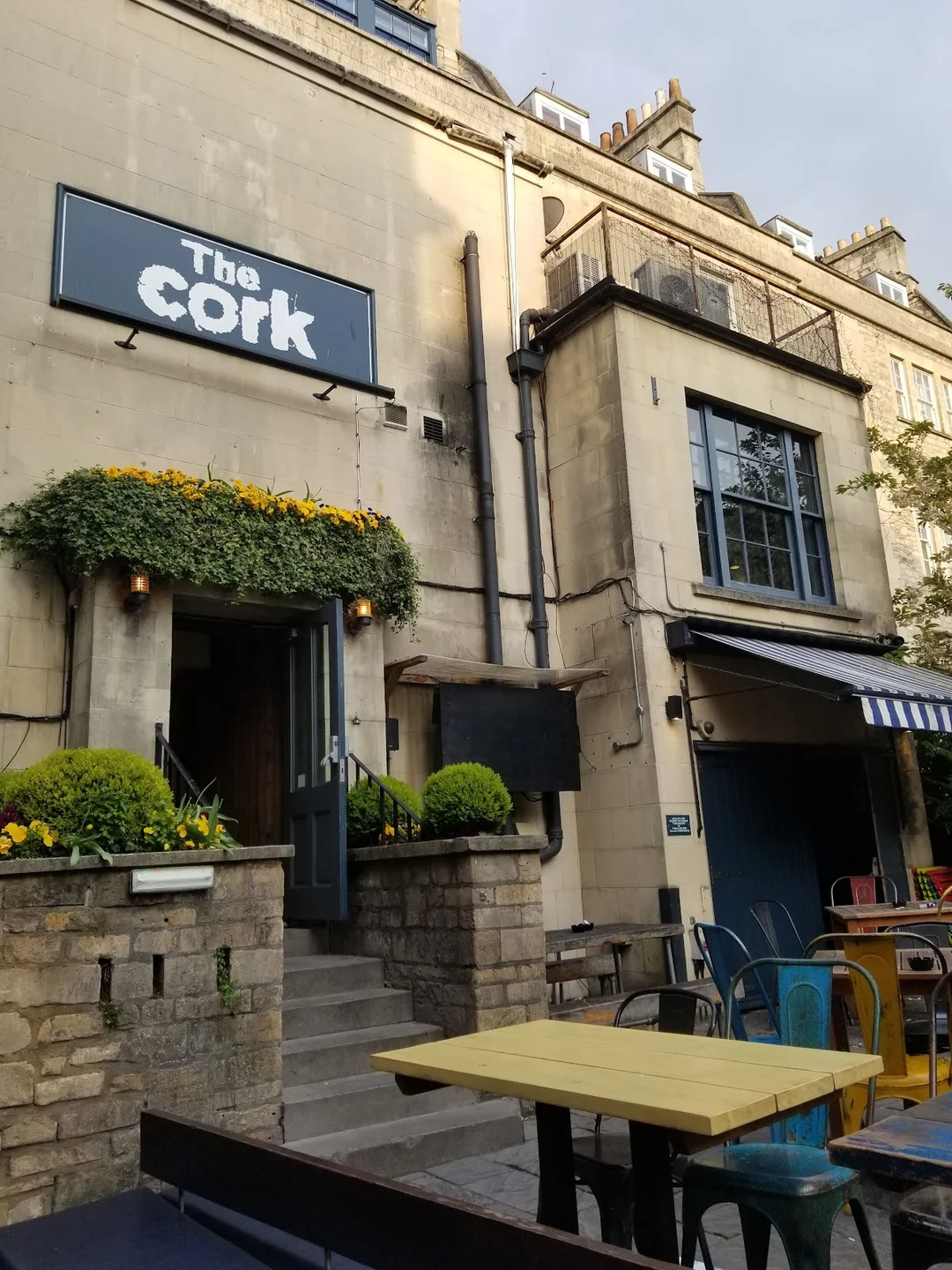 The lively interior or beer garden of The Cork pub in Bath, with people socialising.