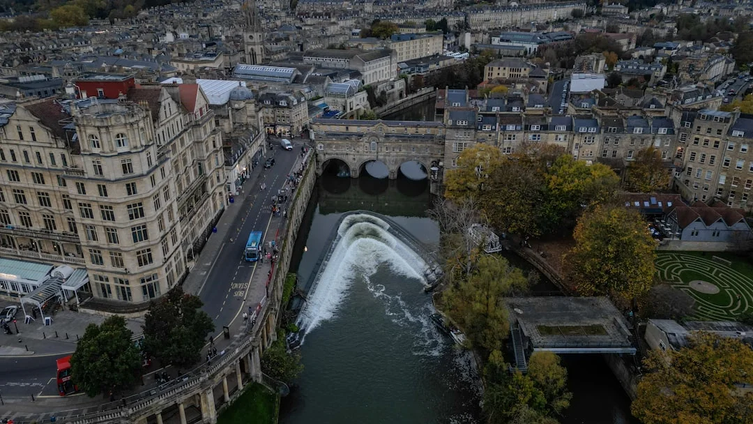 Aerial Bath cityscape showing River Avon, Pulteney Bridge, a weir, and historic buildings with autumn trees